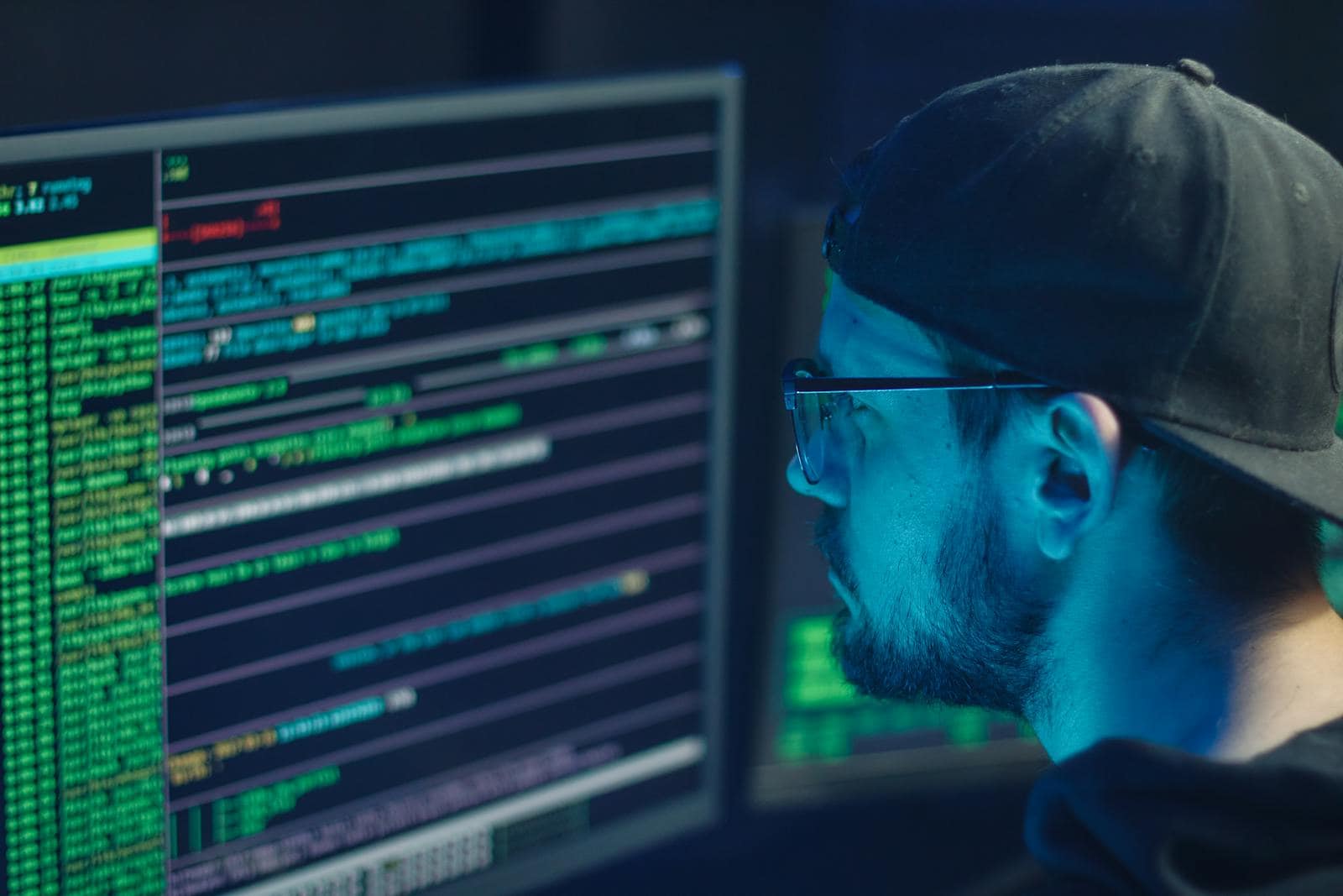 Malware Detection, A cybersecurity expert inspecting lines of code on multiple monitors in a dimly lit office.