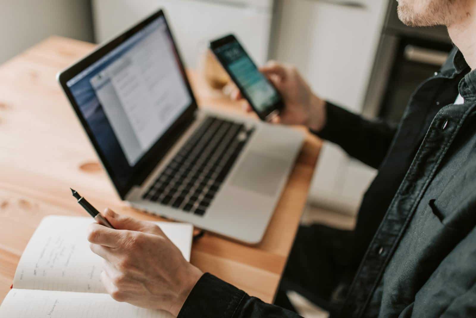 WhatsApp for Advertising, A person multitasking with a laptop and smartphone at a wooden desk.